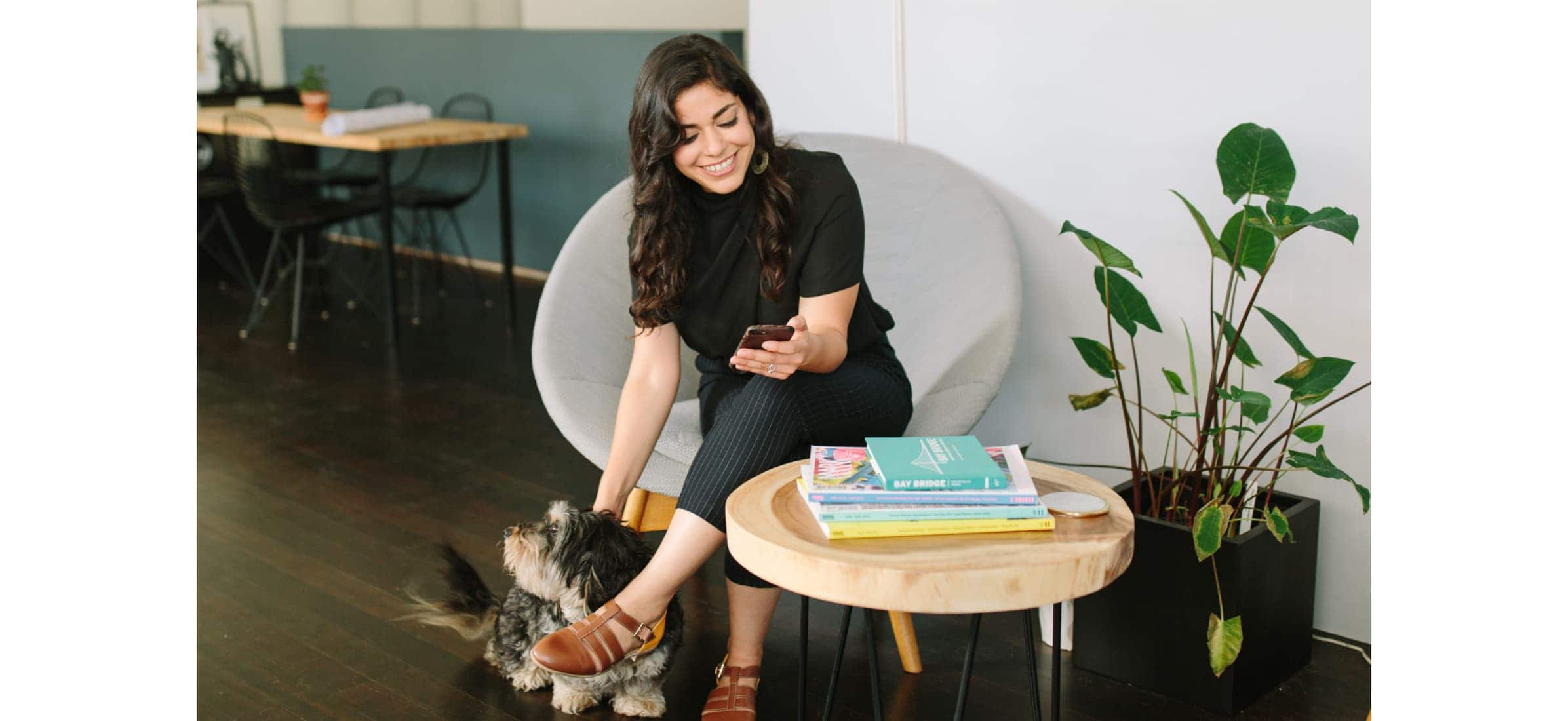 Nastaran sitting in the waiting area of her studio, petting a dog whilst on the phone.